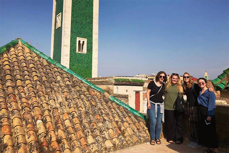 4 students take a picture together next to tiled roof
