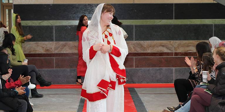 smiling woman walks down fashion show catwalk wearing white and red Arabic fashion